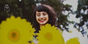 Jeune femme brune en train de sourire face à des fleurs jaunes