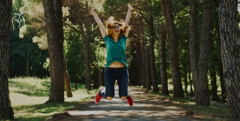 Jeune femme dans une forêt en train de sauter avec les bras en l'air