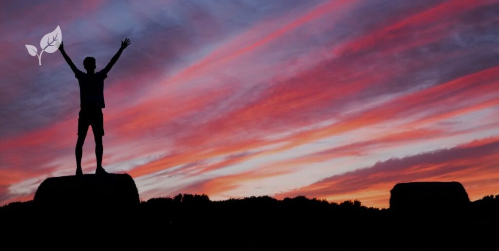 Homme levant les bras au ciel face au coucher du soleil