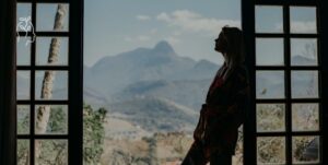 jeune femme adossée à sa baie vitrée et regardant le paysage montagneux au dehors