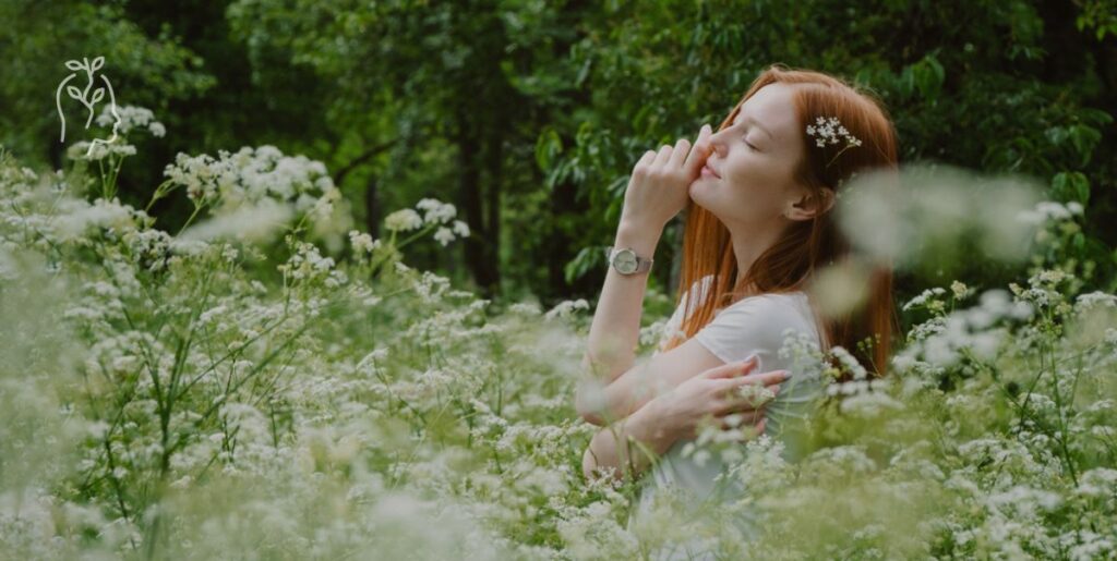 Jeune femme rousse dans un champ en train de sentir une fleur