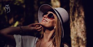 jeune femme avec un chapeau et des lunettes de soleil en train de sourire