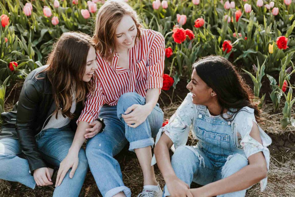 trois jeunes filles assises dans un jardin fleuri en train de rire ensemble