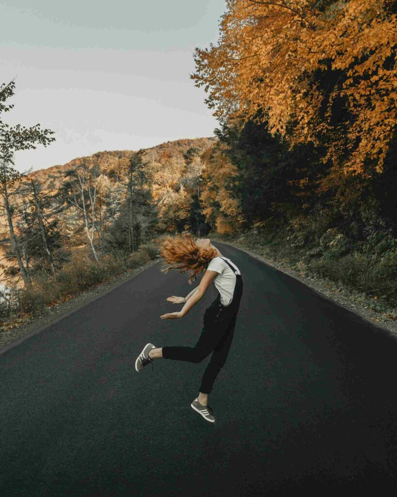 jeune femme heureuse en train de sauter au milieu d'une route